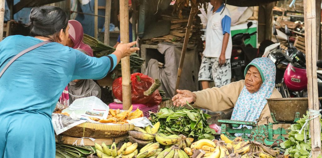 A woman in blue shirt is buying local bananas from a vendor at traditional market.