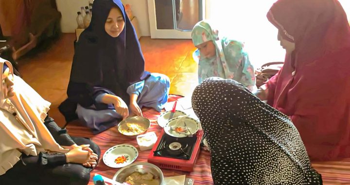 four hijabi women and one child around a stove and several bowls