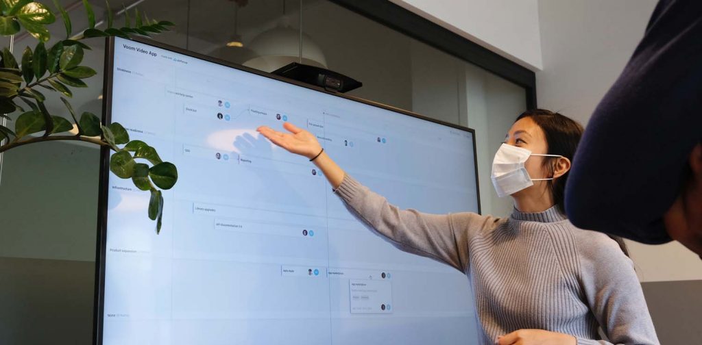 a woman in front of a screen presenting a plan at a meeting