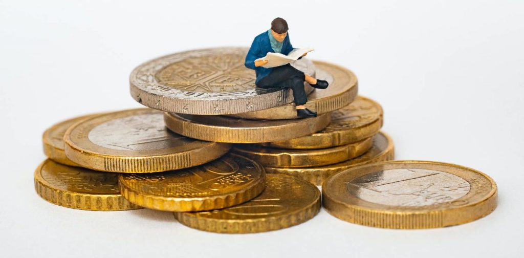 miniature of man reading newspaper, sitting on top of piled coins