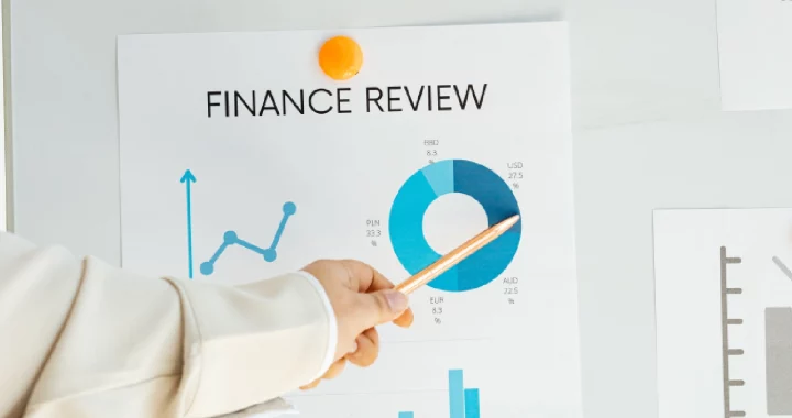 a hand pointing a pencil at charts titled “Finance Review” plastered on a whiteboard